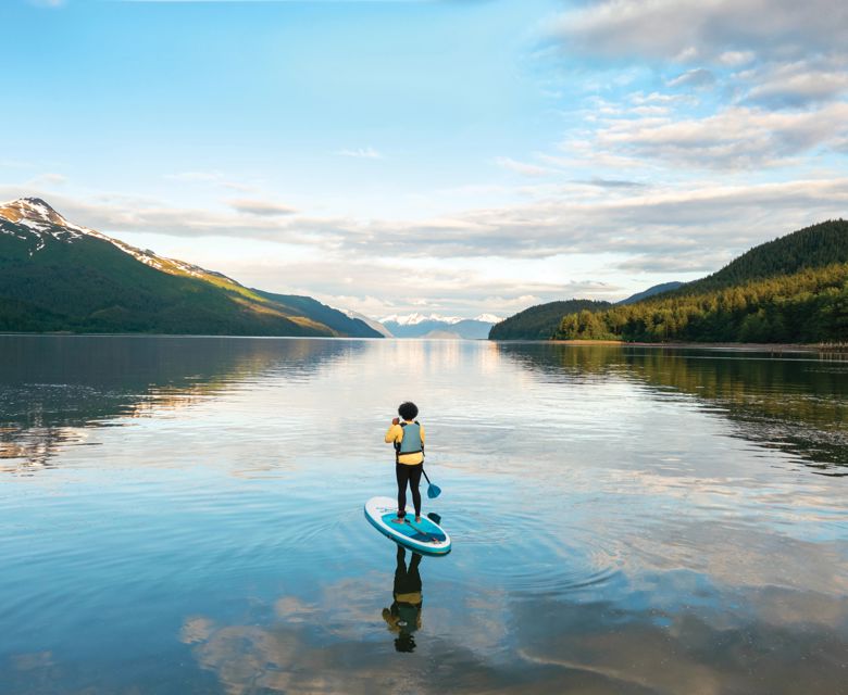 Woman paddleboarding on a glassy water lake on Alaska