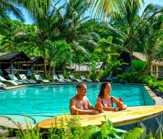 Two people sitting by the pool drinking out of coconuts